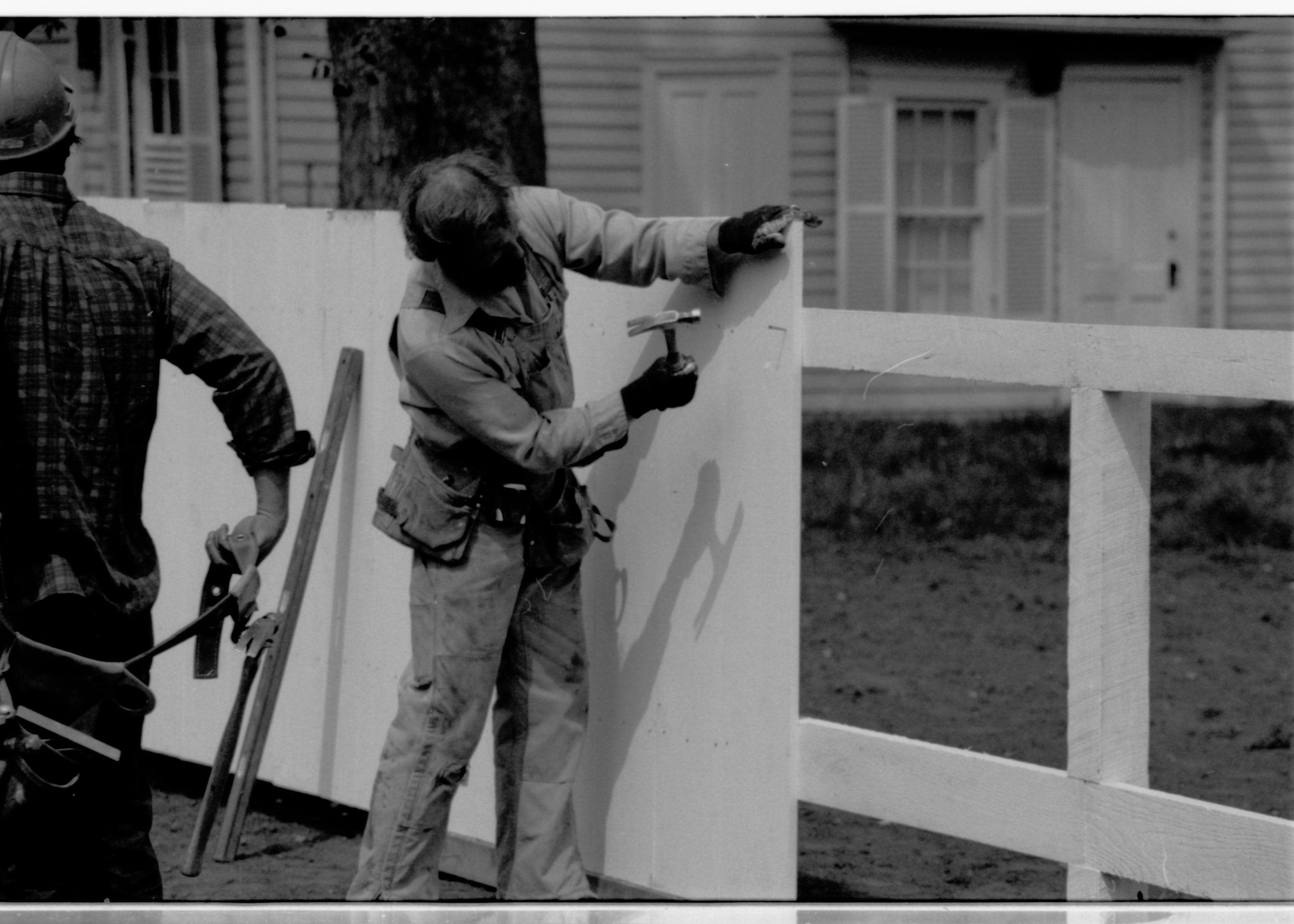 Two workers building fencing along the north line of the Lincoln Home lot. Corneau house (pre-move) in the background. Photographer facing northwest.