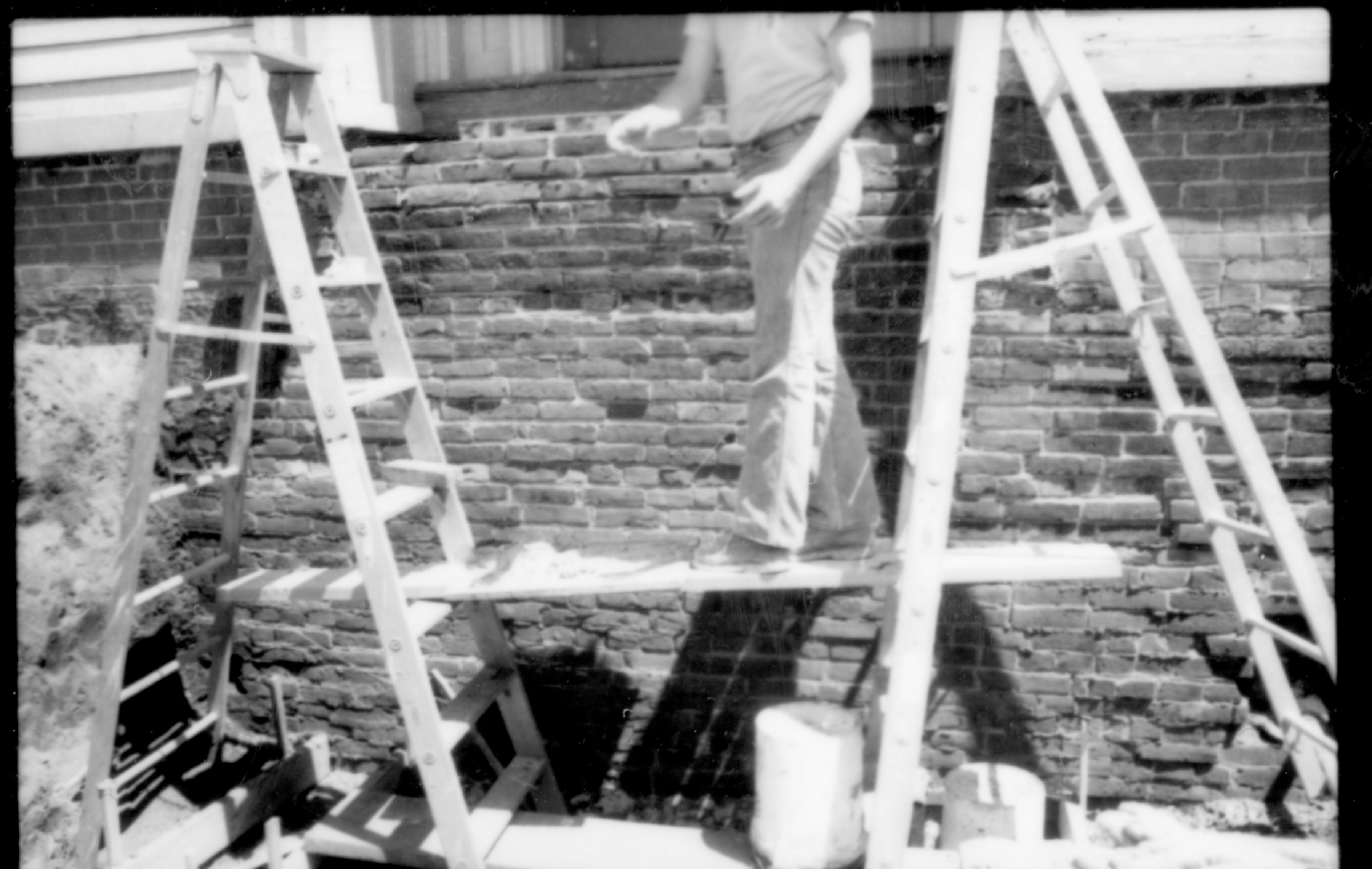 A worker and ladders in a pit located in front of the retaining wall of the front entrace door of the Lincoln Home. Photographer facing east.