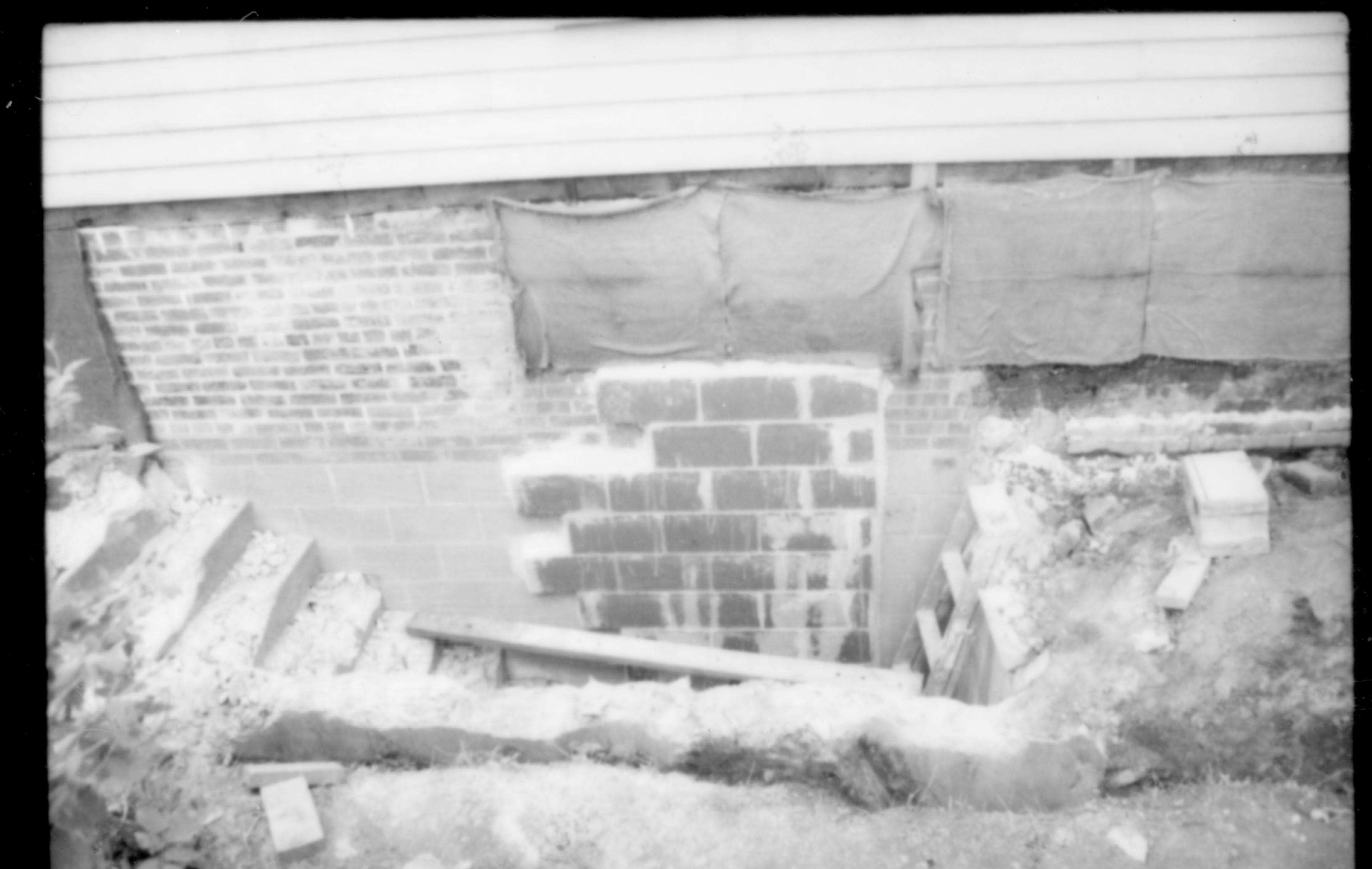 View of the demolition work on the north basement steps, and repairs to the basement and foundation wall during the 1987-88 restoration. Photographer facing south.