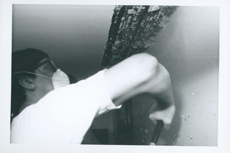 Worker removing plaster from the ceiling of the Lincoln Home, probably in the 2nd floor Back Hall. Note the exposed lath work. Photographer facing west.