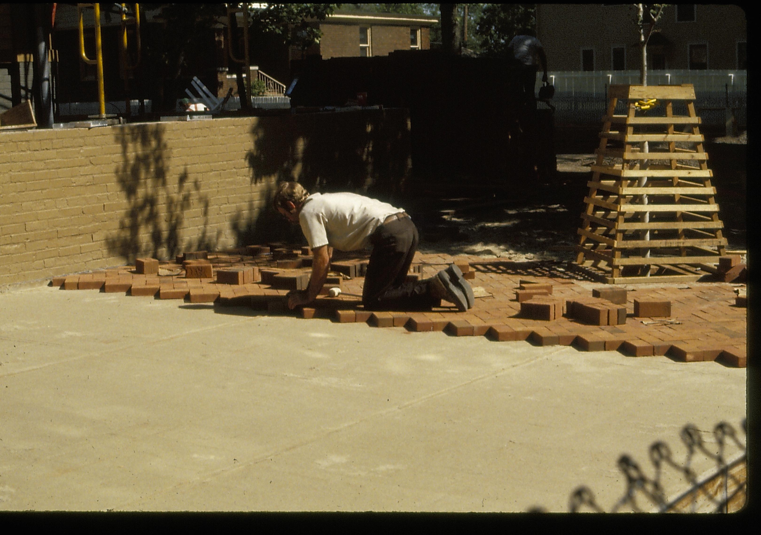 Bricklayer setting the bricks for the plaza in front (west) of the Lincoln Home during the 1987-88 Restoration. Retaining wall in near background. Pre-move Arnold House in middle background; Cook House in right background. Photographer facing south east.