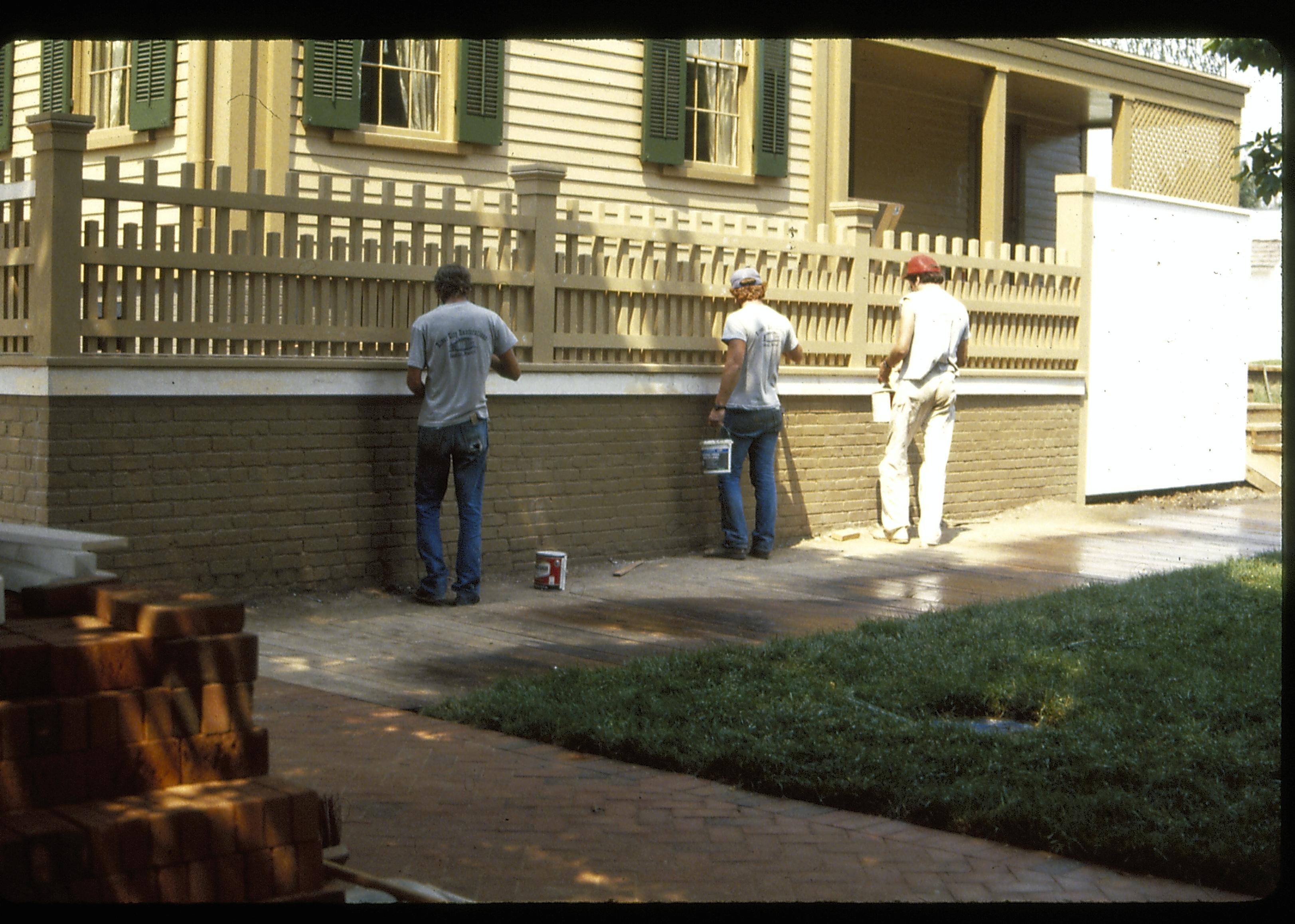 Three workers painting the east retaining wall fence of the Lincoln Home during the 1987-1988 restoration. Photographer facing north east.