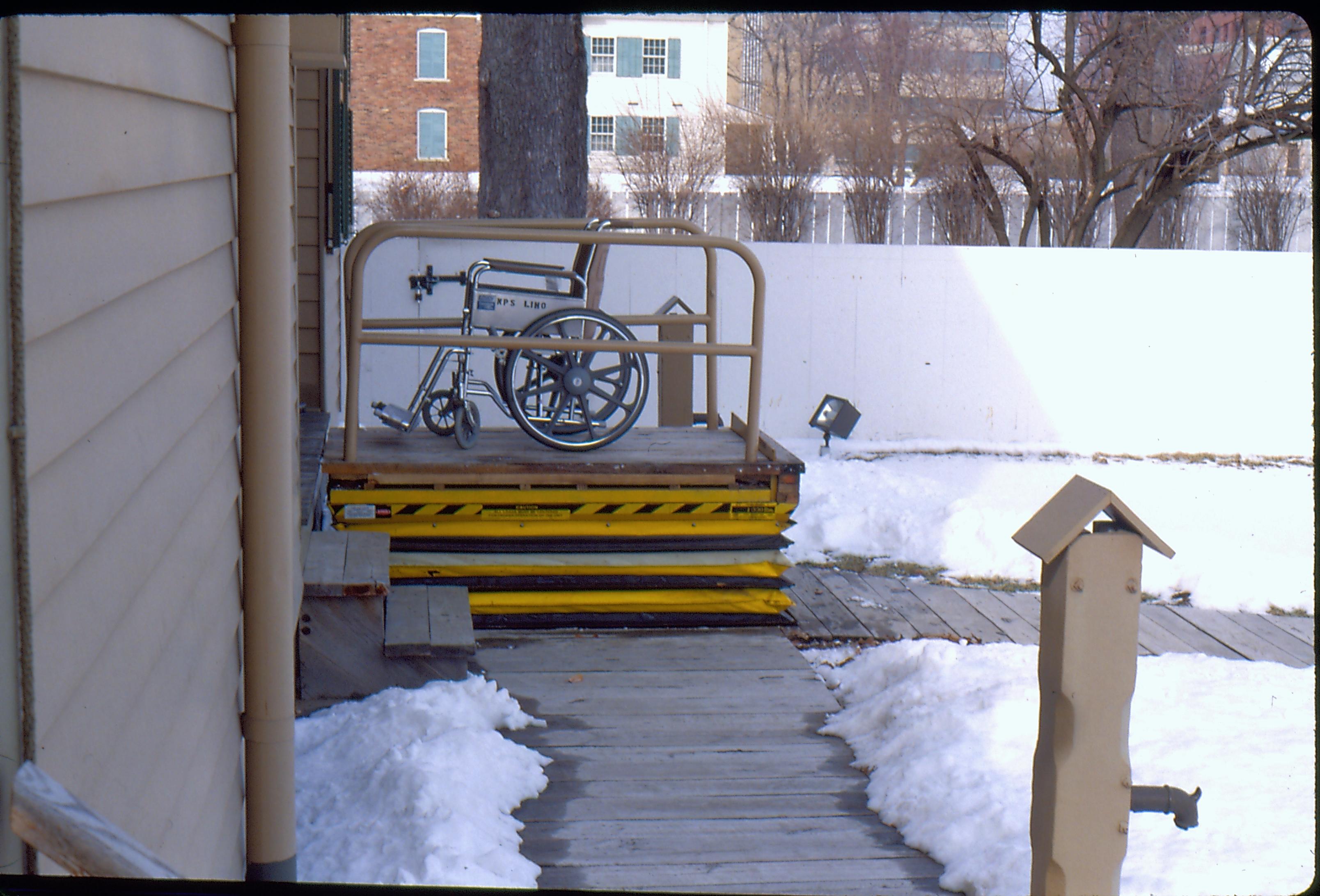 Wheelchair lift of the Lincoln Home, at full height, with empty wheelchair. Snow on the ground. Photographer facing north.