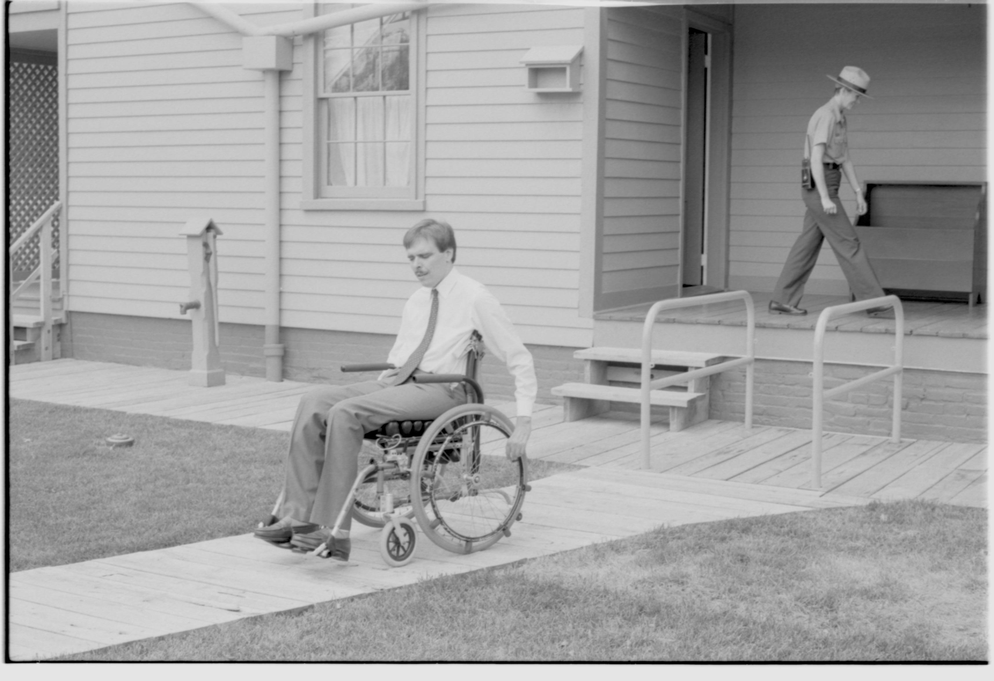 A man in a wheelchair exiting the Lincoln Home wheelchair lift. A staff member is seen walking on the Lincoln Home east porch. Photographer facing south west.