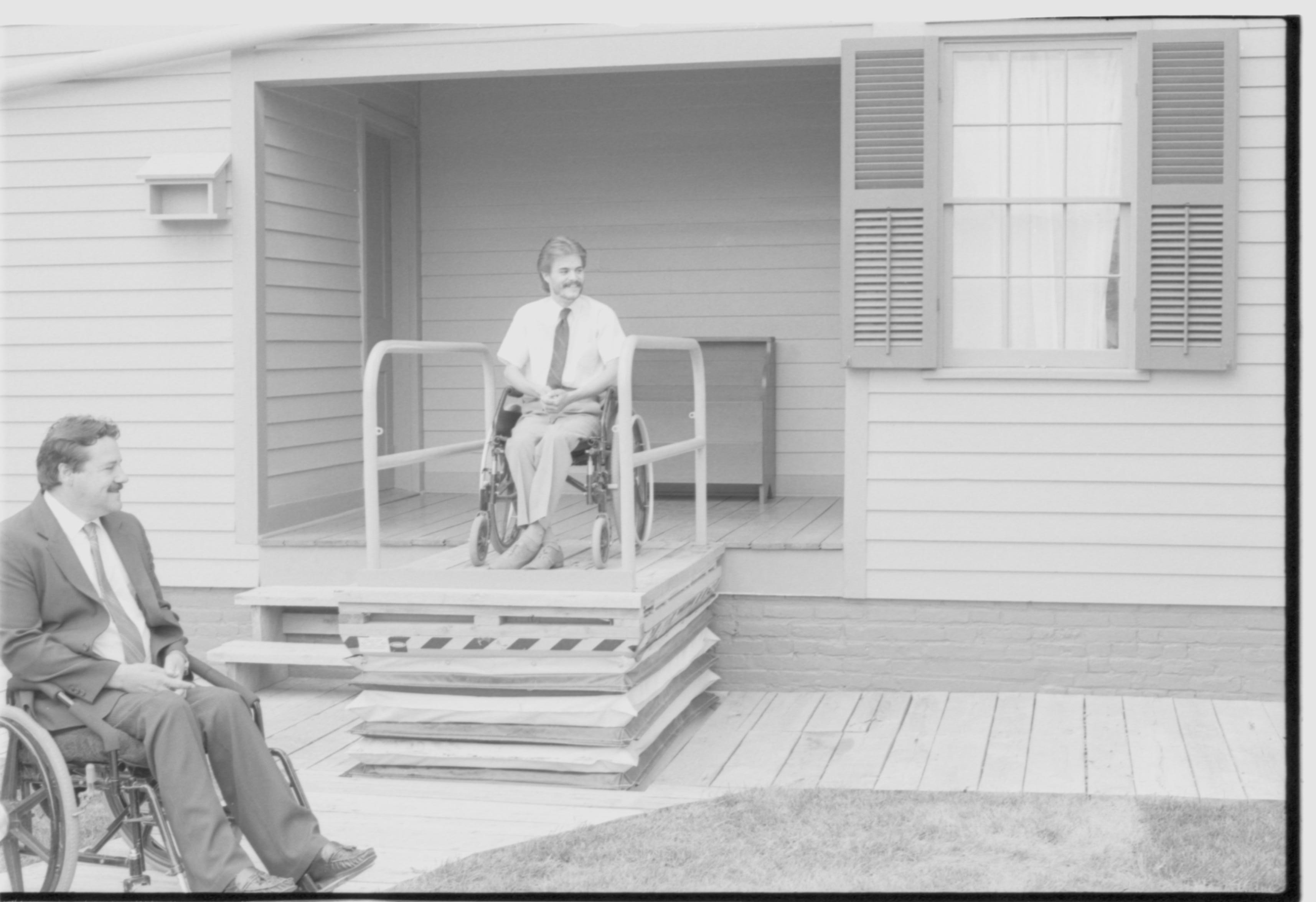 Lincoln Home wheelchair lift, at full height. One man in wheelchair on lift, facing away from Lincoln Home, with second man in wheelchair at ground level. Photographer facing south west.