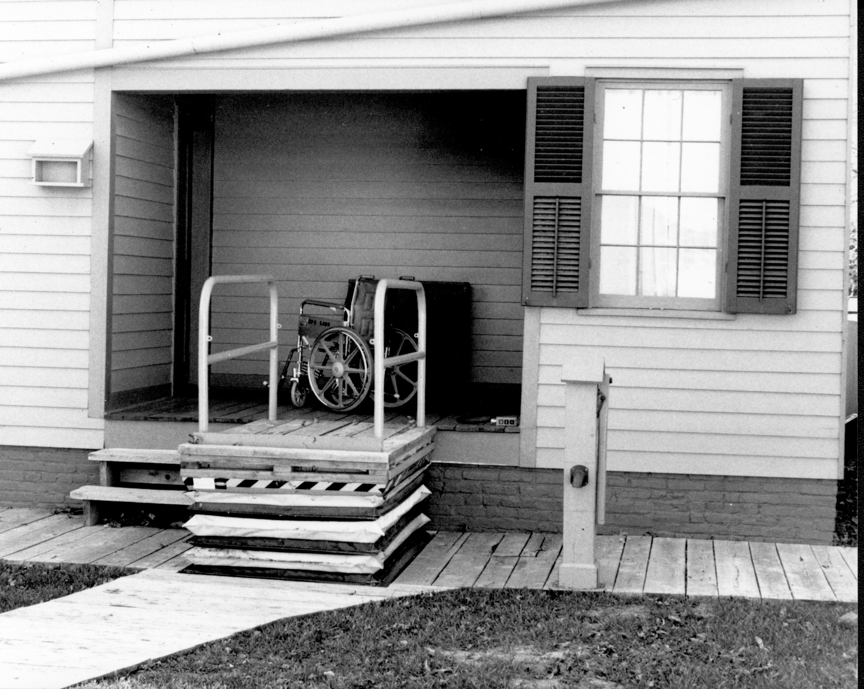 Lincoln Home wheelchair lift, fully extended, with empty wheelchair on east porch. Photographer facing west.