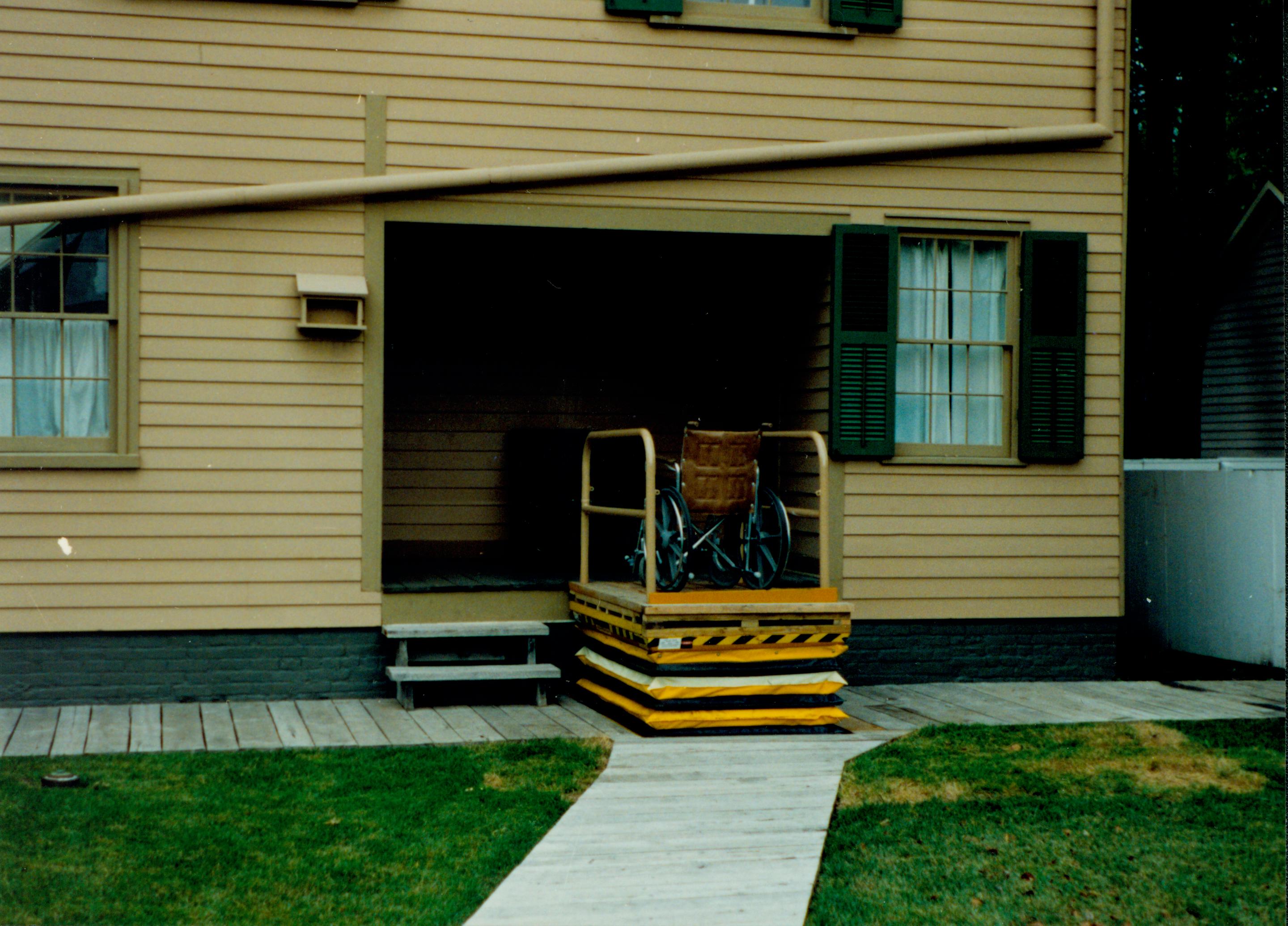 Lincoln Home wheelchair lift at full height, with empty wheelchair. Photographer facing west.
