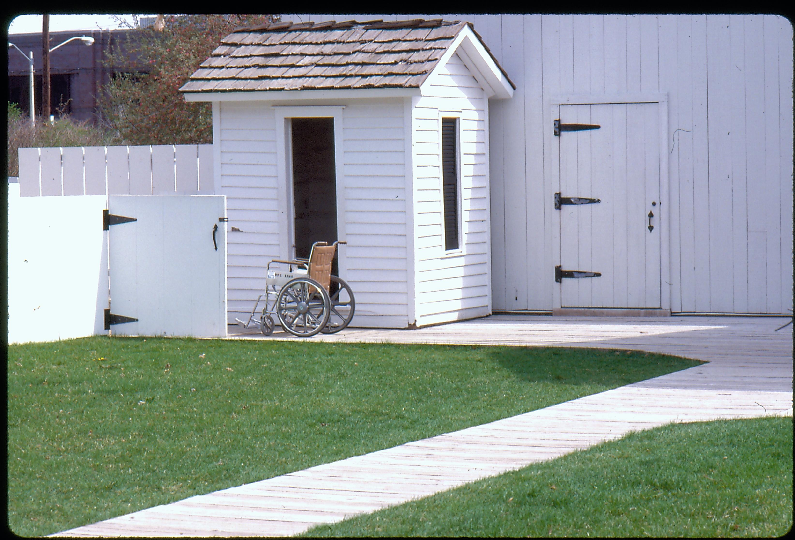 Back yard of the Lincoln Home, facing north east. A wheelchair sits near the privy and north east access gate to the yard.