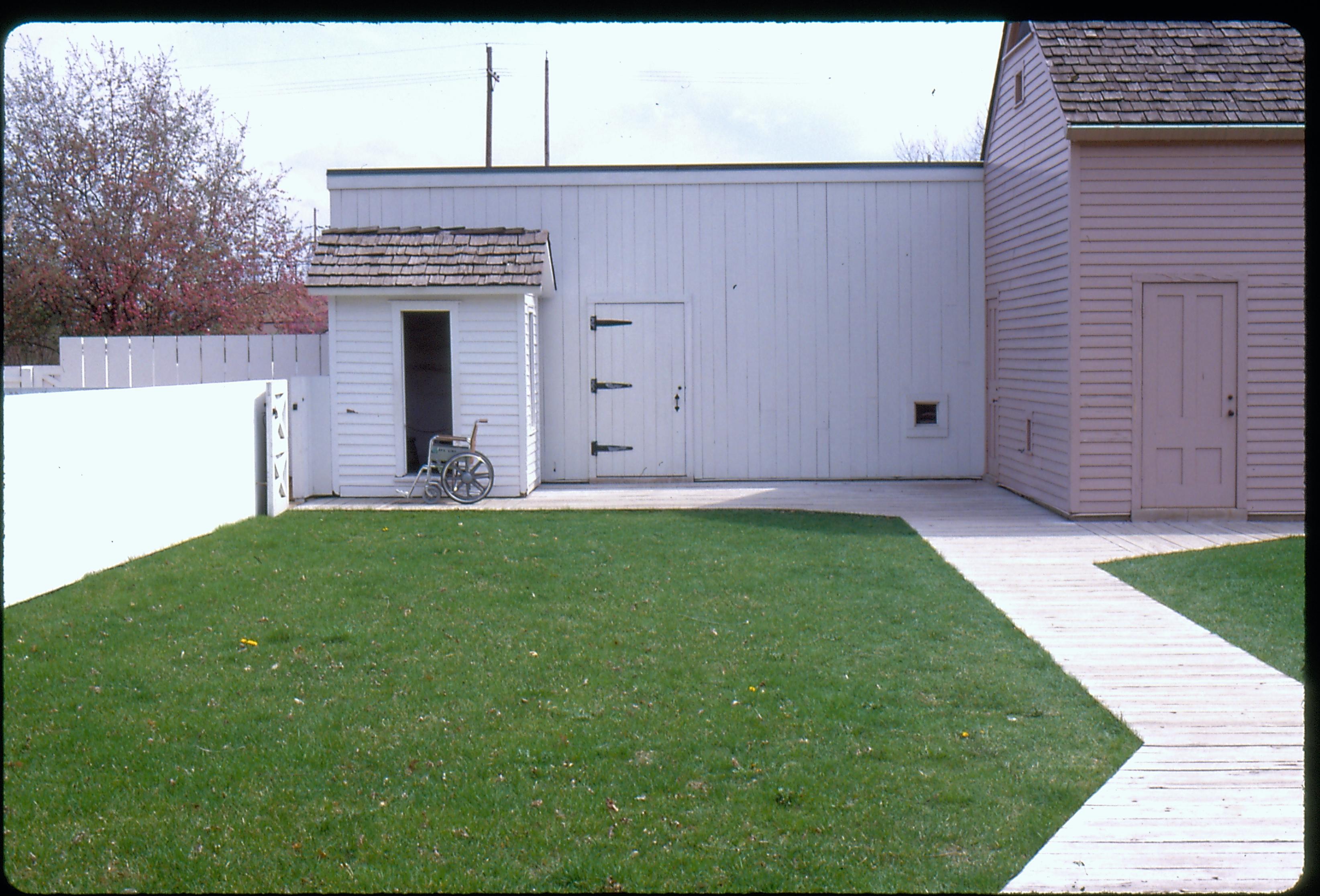 Back yard of the Lincoln Home, facing east. A wheelchair sits near the privy and north east access gate to the yard.