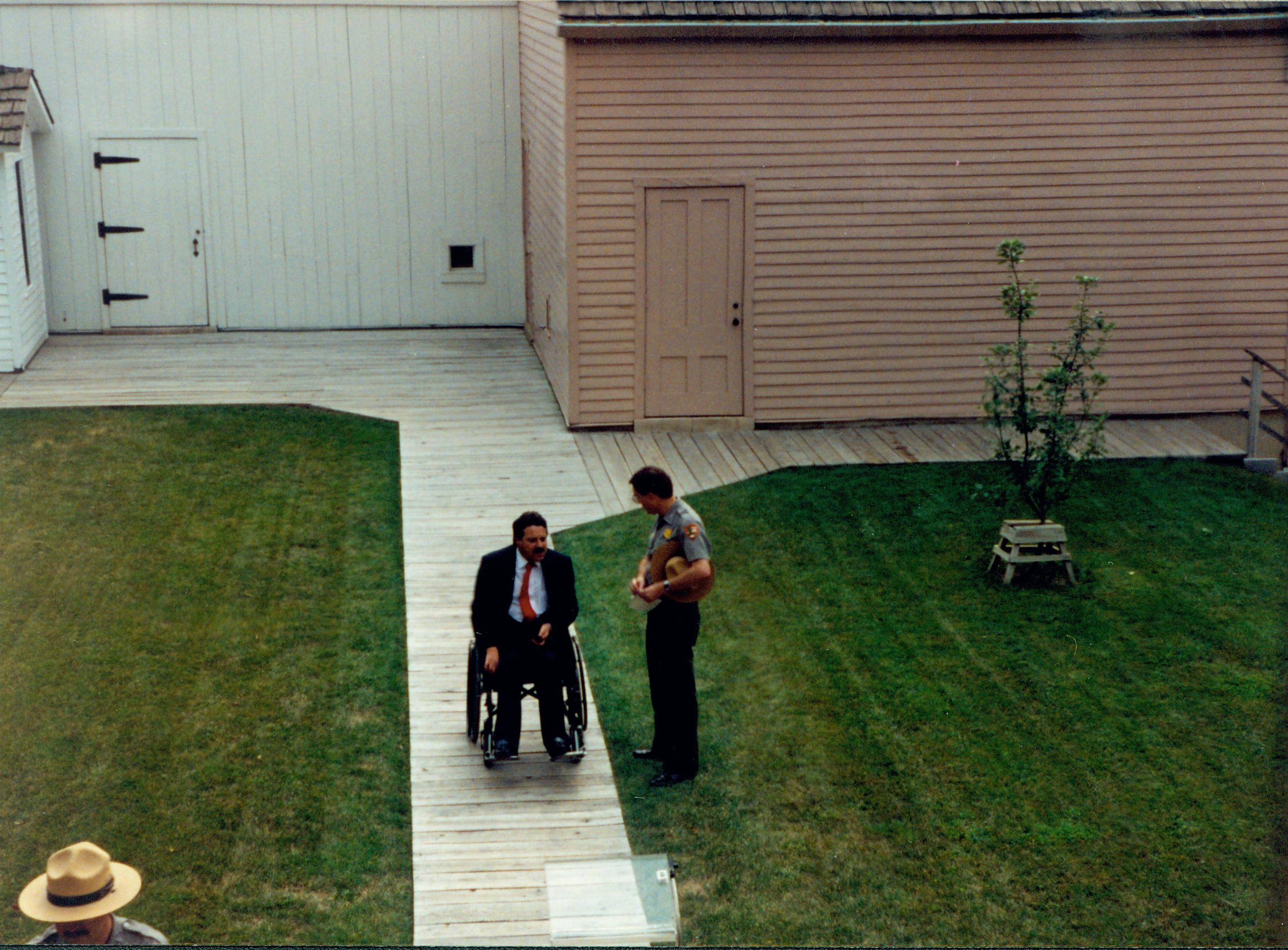 A man in a wheelchair waits on the Lincoln home back yard boardwalk while chatting with a Lincoln Home staff member. Photographer facing east.