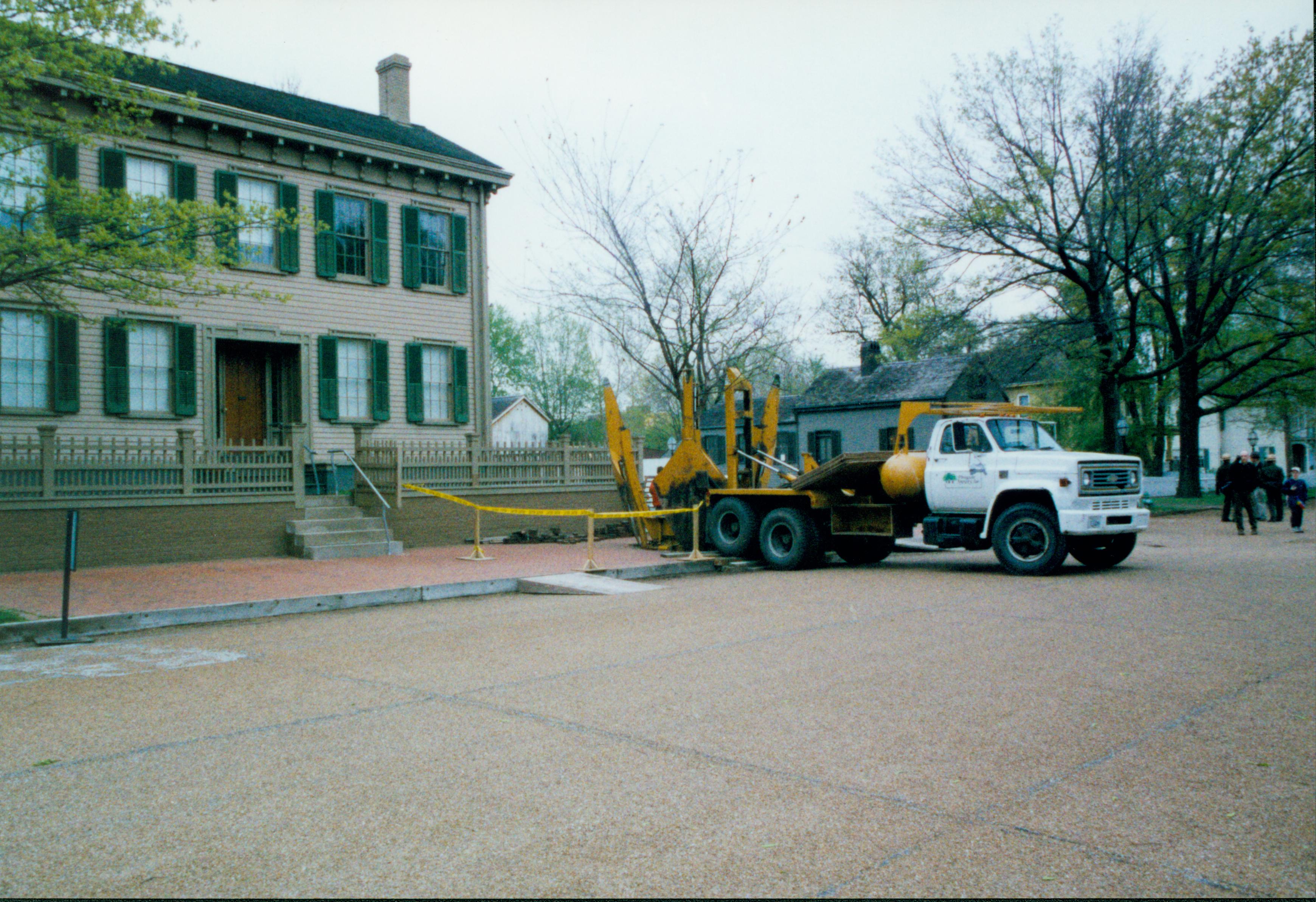 Elm tree replacement - Pleasant Nursery prepares to remove large elm tree from brick plaza in front of Lincoln Home.  Visitors talk to rangers in background right. Arnold, Cook and Robinson Houses visible in background behind Pleasant Nursery truck Looking Southeast from 8th Street Elm tree, Lincoln Home, Arnold, Arnold Barn, Cook, Robinson, 8th Street, brick plaza, Pleasant Nursery