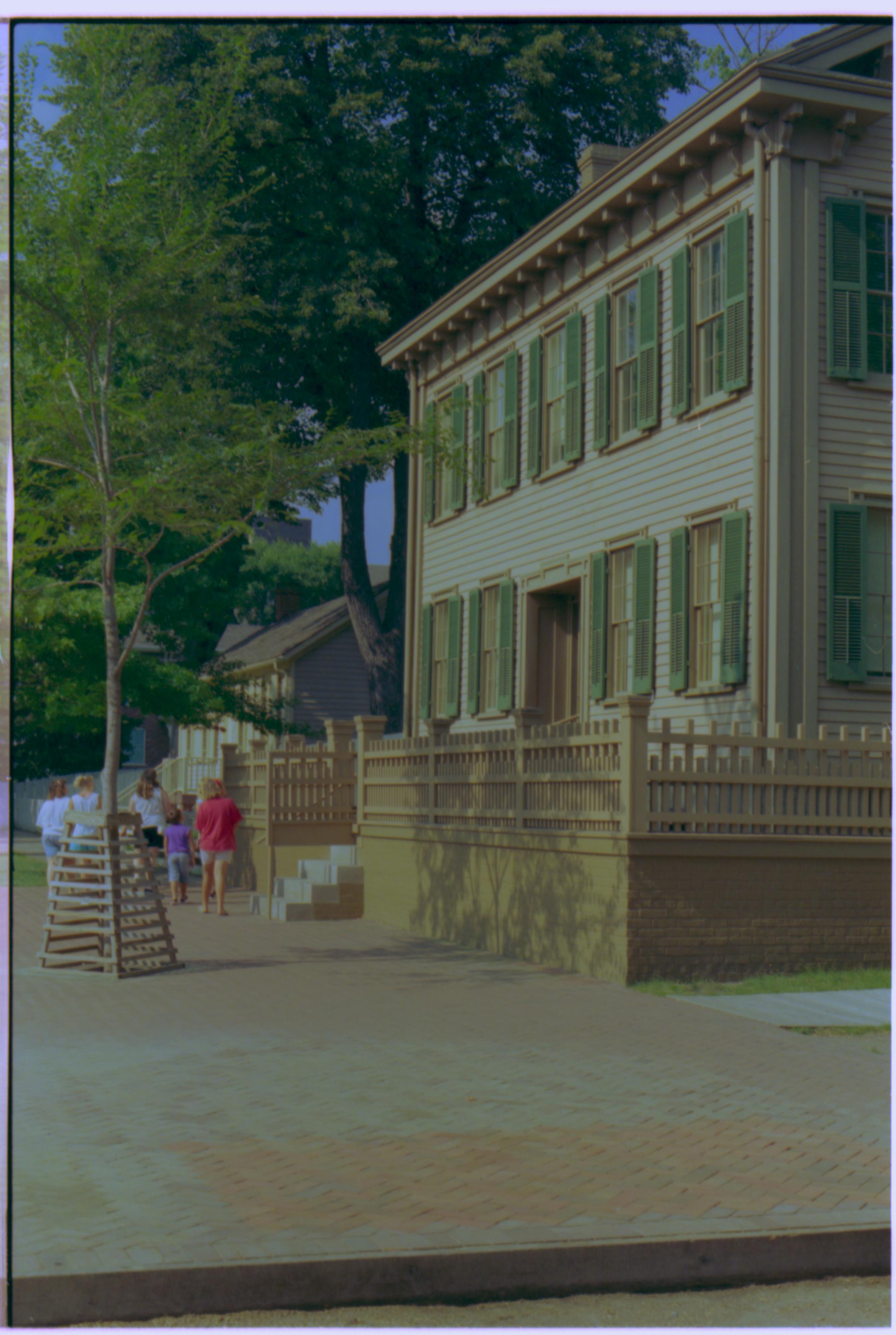 A group of visitors walking on the brick plaza west of the Lincoln Home. Pre-move Corneau House in background. Summer. Photographer facing north east.