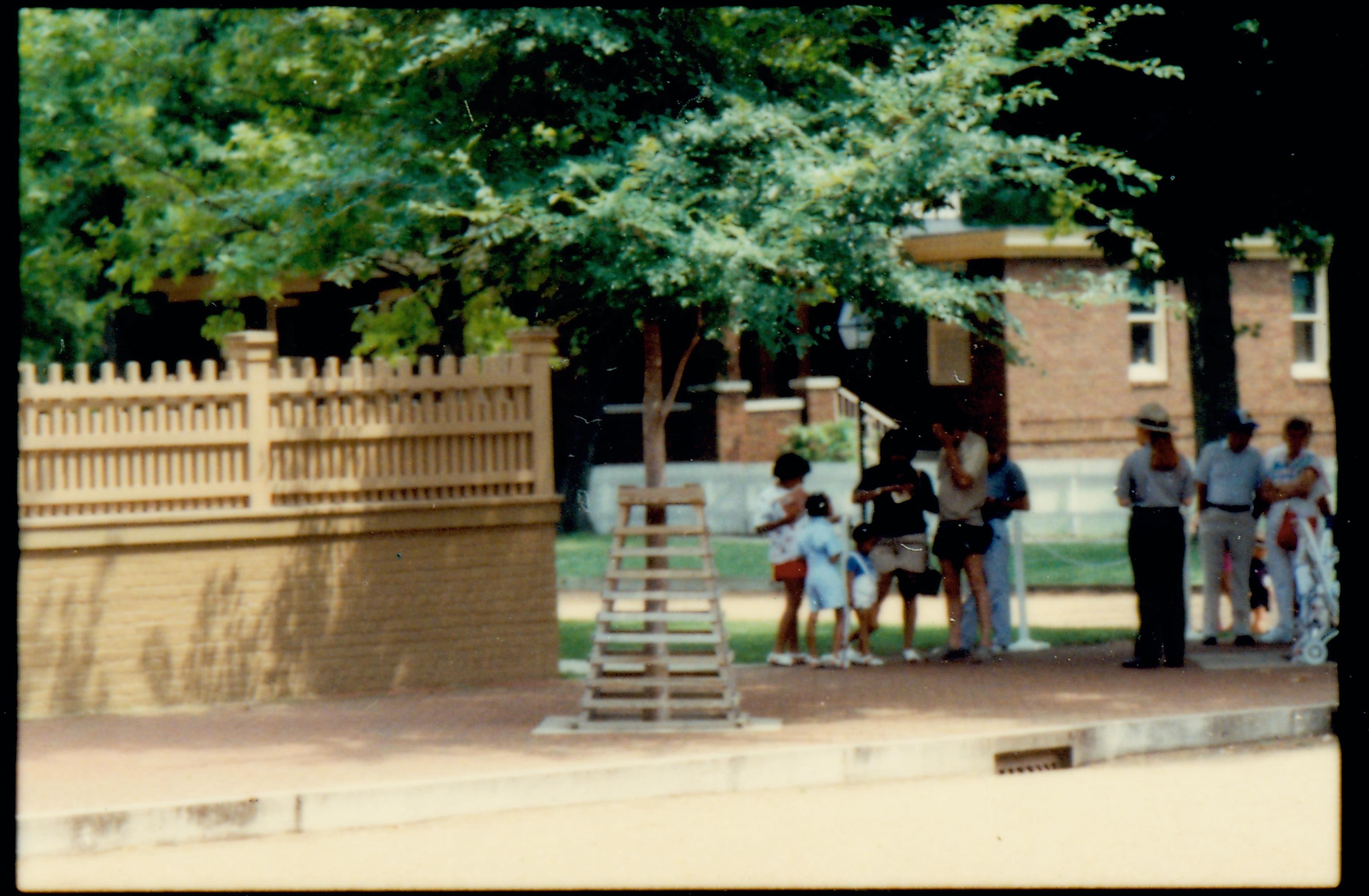 A ranger with a group of visitors on the brick plaza south west of the Lincoln Home. Summer. Unrestored Arnold House in background. Photographer facing south east.