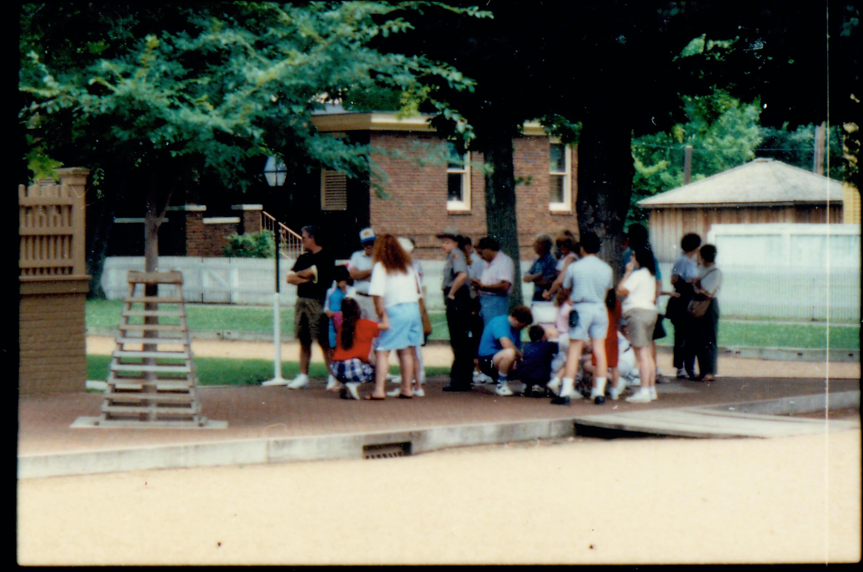 A ranger with a group of visitors on the brick plaza south west of the Lincoln Home. Summer. Unrestored Arnold House in background. Photographer facing south east.