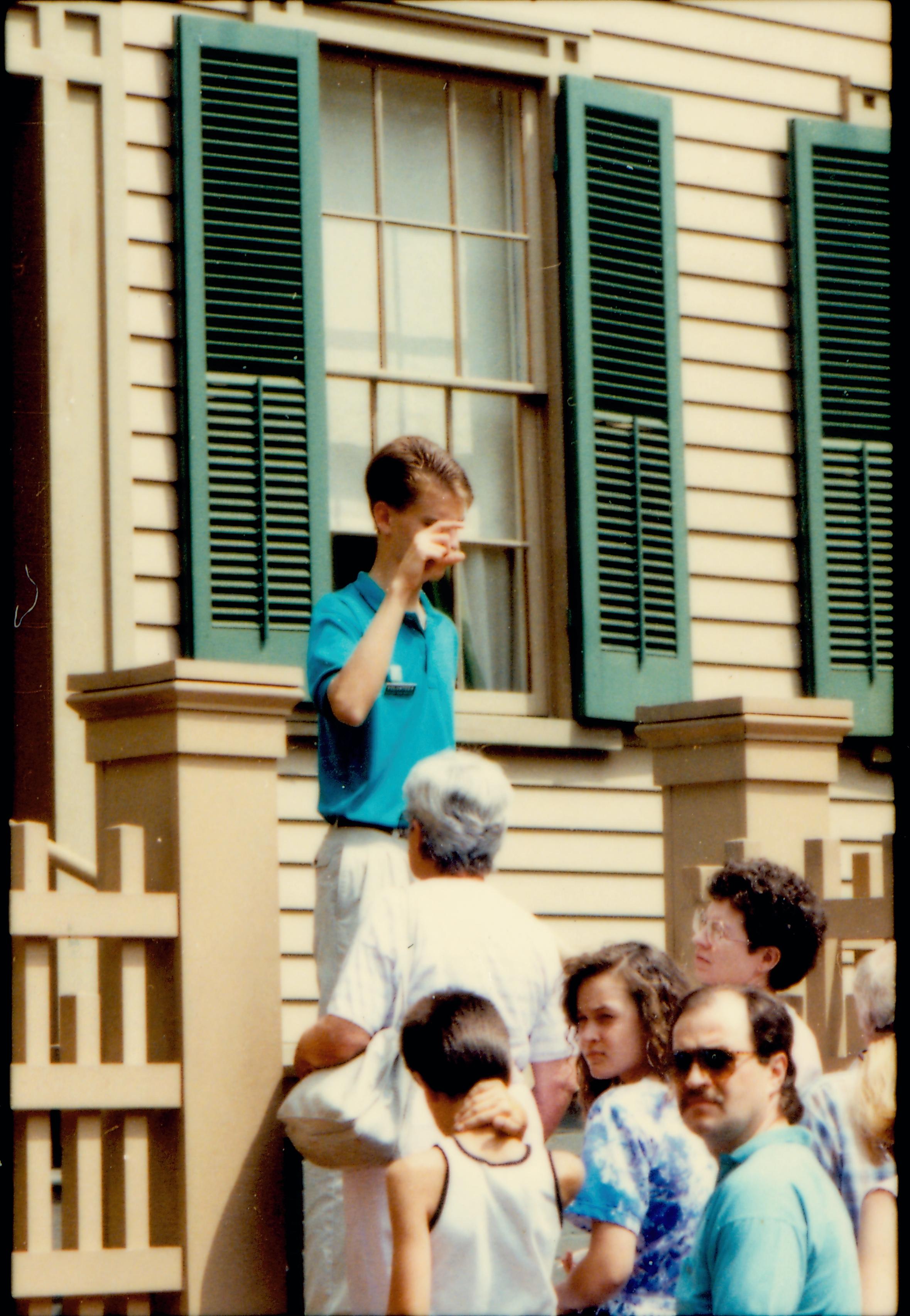 Non-uniformed park staff or volunteer speaking to visitors from the front (west) steps of the Lincoln Home. Photographer facing south east.