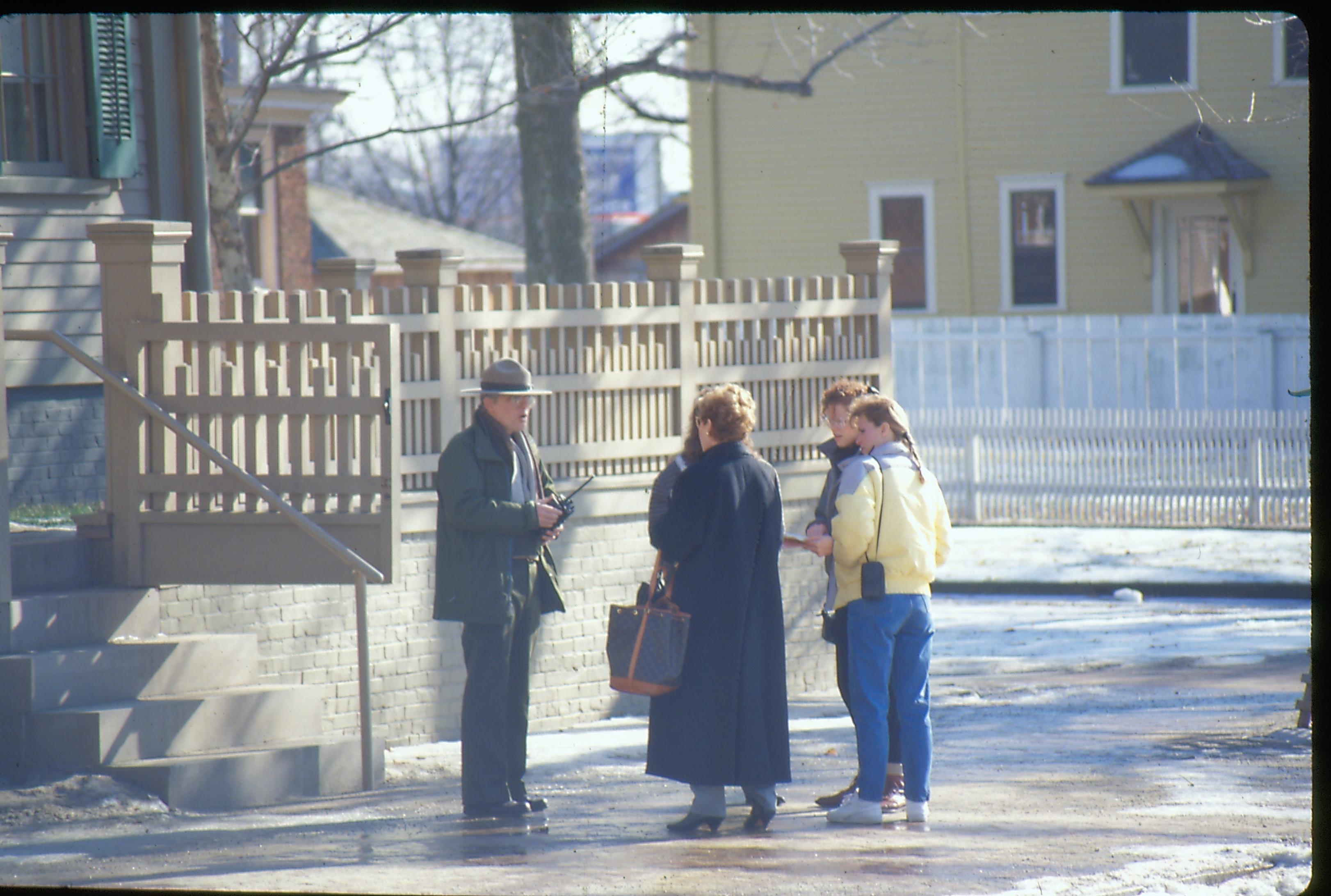 A ranger speaks to a small group of visitors on the brick plaza of the Lincoln Home. The Cook House can be seen in the background. Winter view. Photographer facing south east.