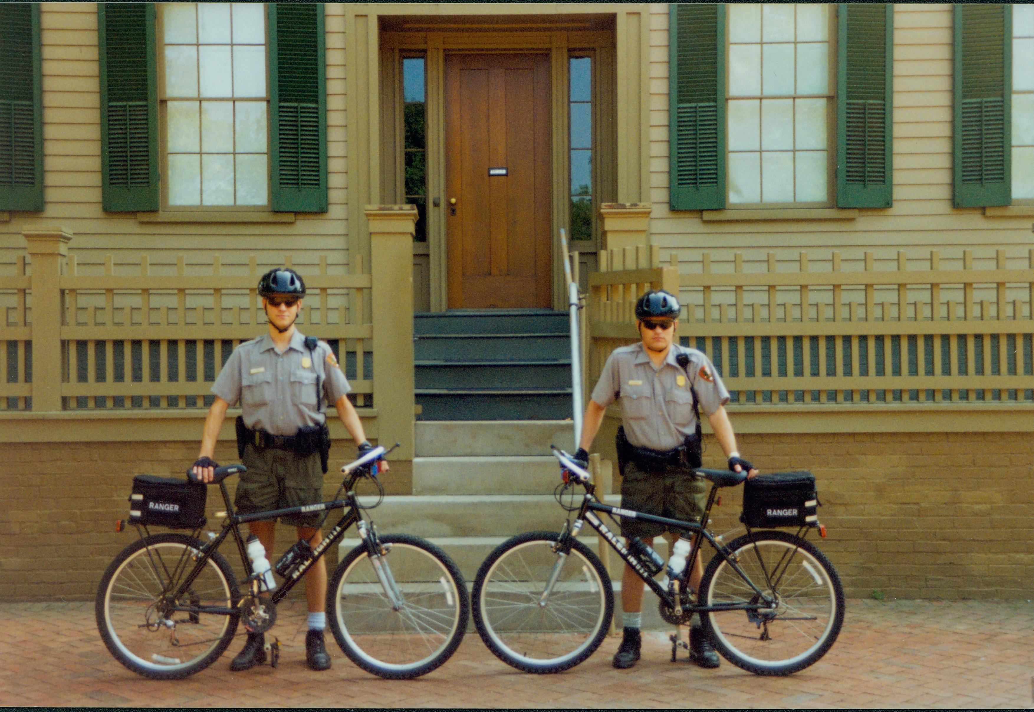 Two law enforcement rangers stand in front of the Lincoln Home with their patrol bicycles. Ranger Jeff Budny stands on the left, while Ranger Rodney Naylor stands to the right. Photographer facing east.