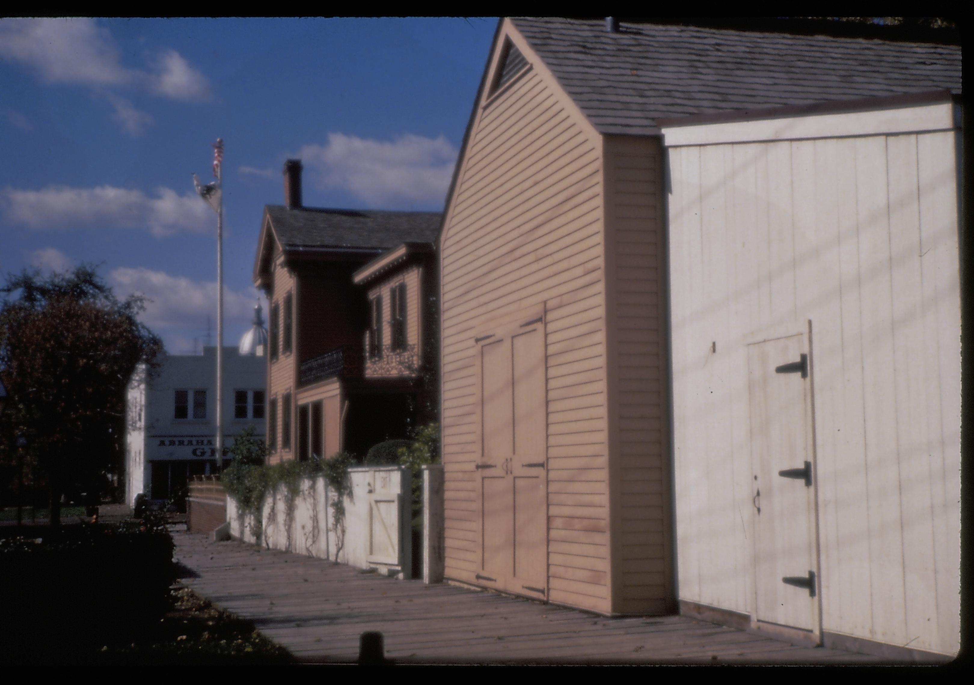 Lincoln Home carriage house and woodshed, with the Lincoln Home in the background. The Gift Shop (formerly the Piggly Wiggly) is in the far background. Photographer facing west.