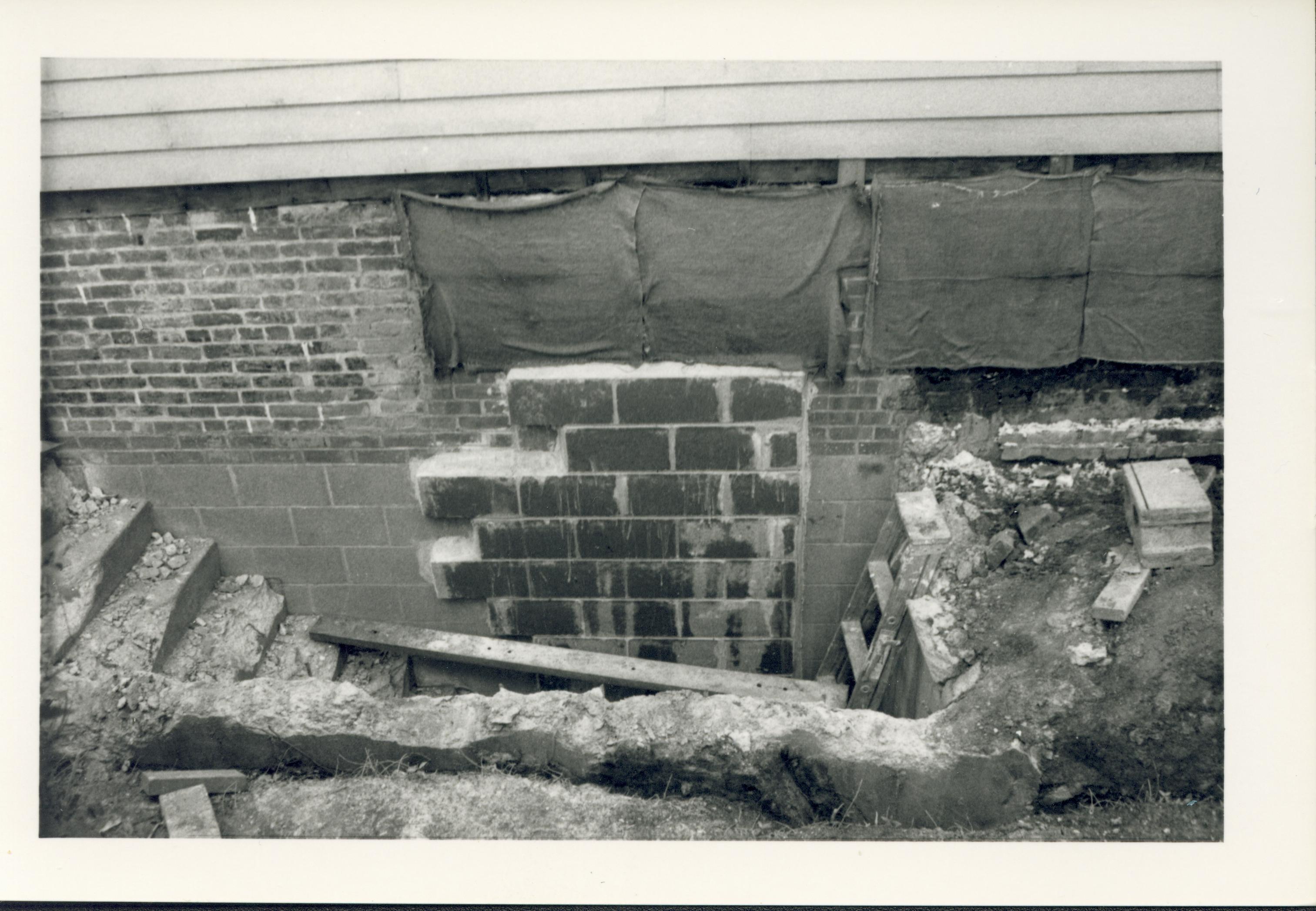 Demolition of the non-historic basement-level north entrance to the Lincoln Home mechanical room/basement. The former doorway is filled with cinderblock, while the stairs and retaining wall are in the process of demolition. Photographer facing south.
