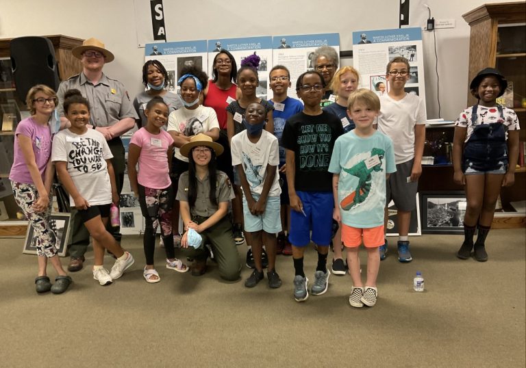 Group of children and two park rangers stand in front of exhibit panels