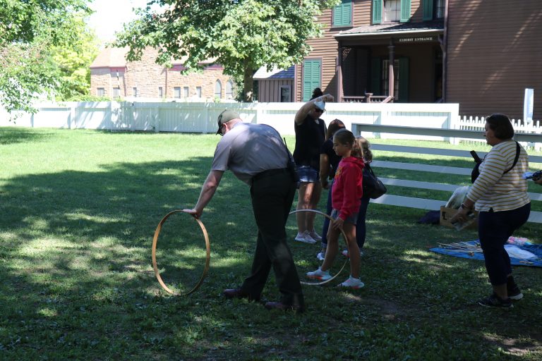 Park Guide, Max Farley, demonstrates the toy of Hoop and Stick for some young visitors.